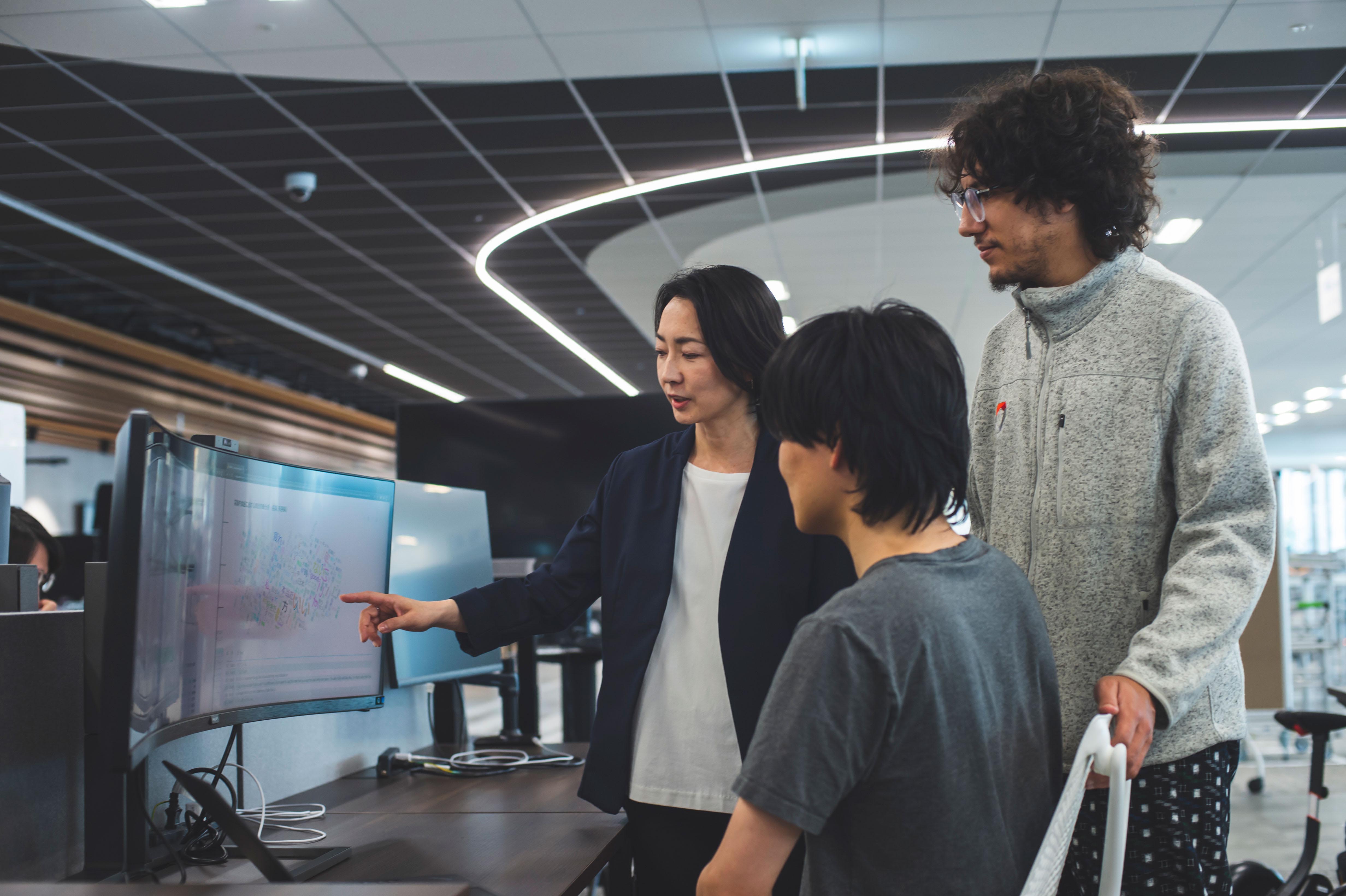 Photo of Suzuka and Marouane from Woven by Toyota talking to a man sitting in front of a monitor